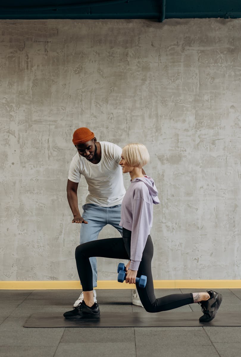 A personal trainer guides a woman doing lunges with dumbbells in a gym setting. Fitness and lifestyle concept.